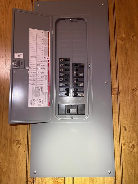 Open electrical panel with circuit breakers and wiring diagram on wooden floor