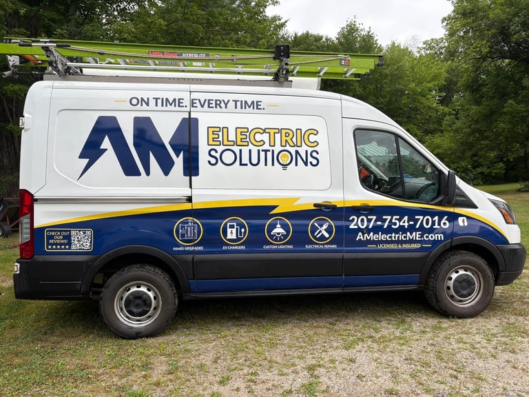 White and blue AM Electric Solutions service van parked on grass with company logo, tagline, phone number, and service icons displayed on the side.