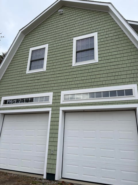 Two-story house with green shingled exterior, white trim, two white garage doors, and upper windows