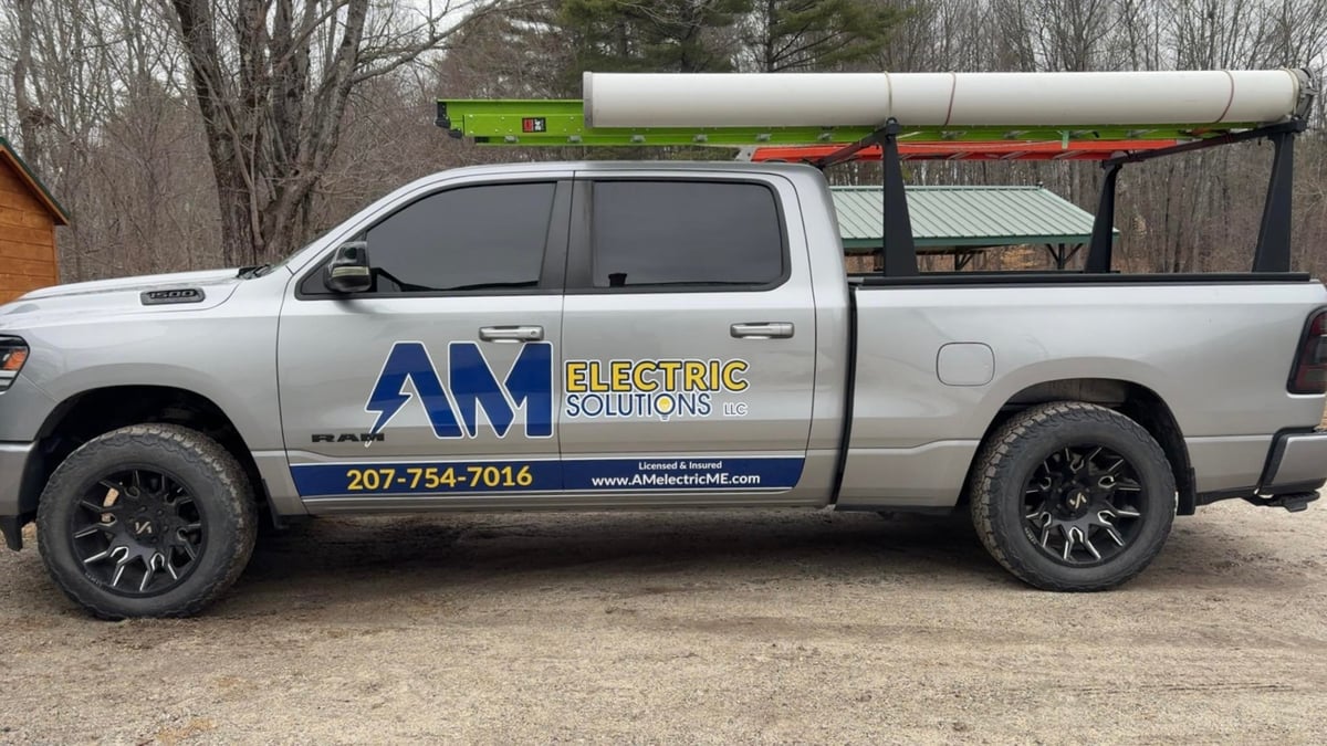 White pickup truck with large white pipe on roof rack and blue AM Directional Solutions logo on side