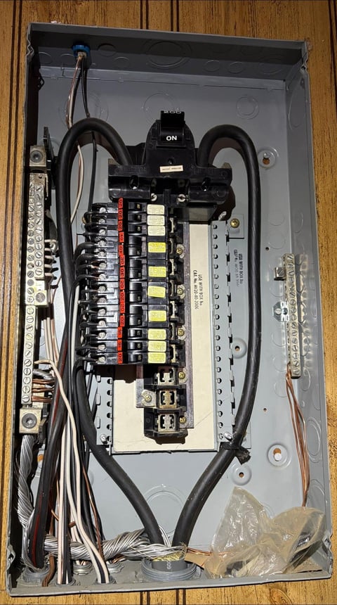 Interior view of an electrical breaker panel box with circuit breakers, wiring, and an ON switch mounted on a wooden surface
