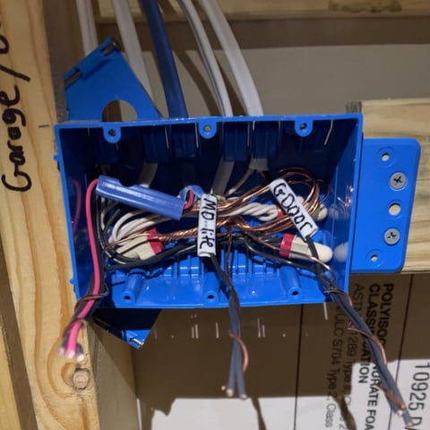 Blue electrical junction box mounted on wooden studs with bundled wires and cable connections inside